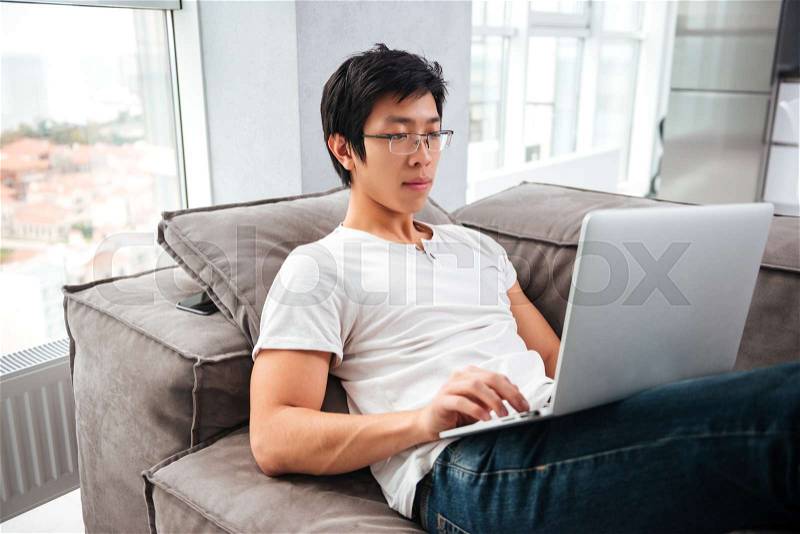 Side view of asian man with laptop on sofa. looking at laptop, stock photo