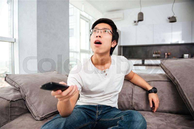 Surprised asian man watching tv on sofa. from below, stock photo