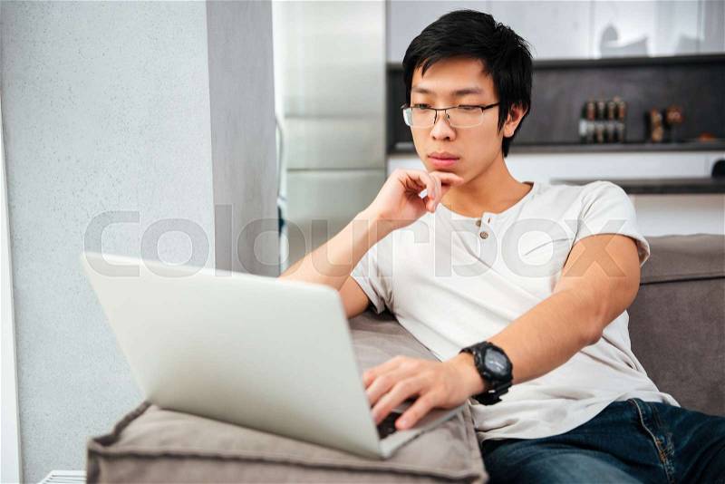 Serious asian man with laptop on sofa. looking at laptop, stock photo