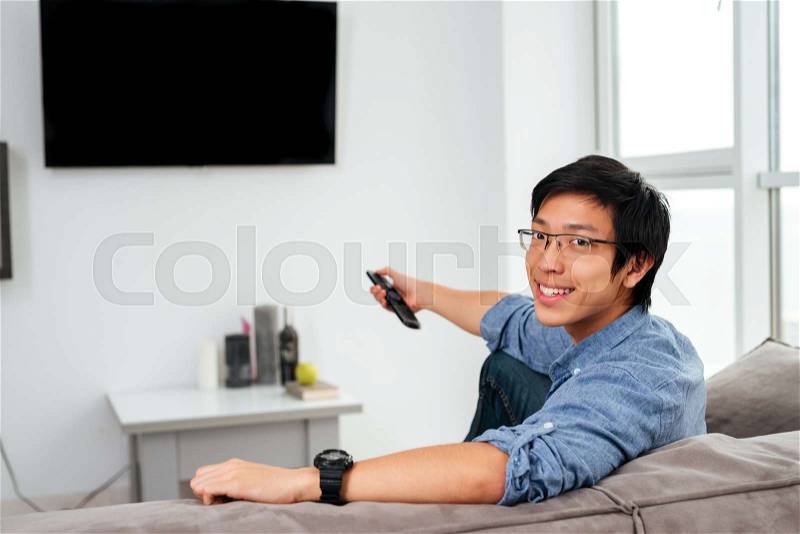 Young asian man in shirt watching tv on sofa. looking at camera, stock photo