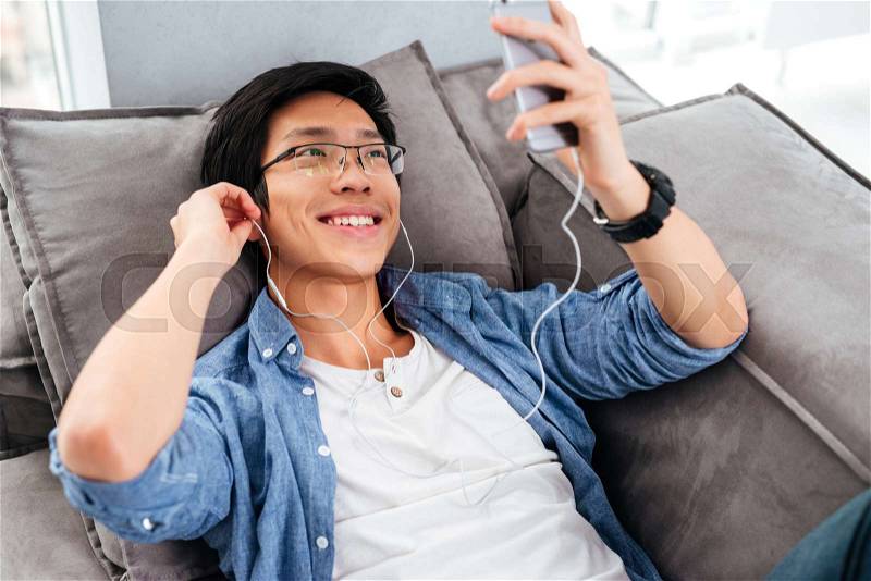 Happy asian man in shirt with phone on sofa. listening music, stock photo