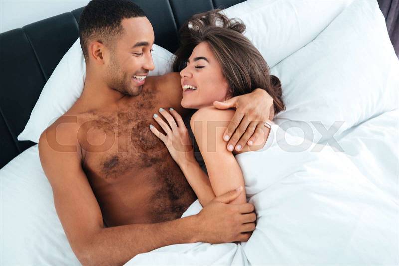 Cheerful young couple laughing and hugging in bed at home, stock photo