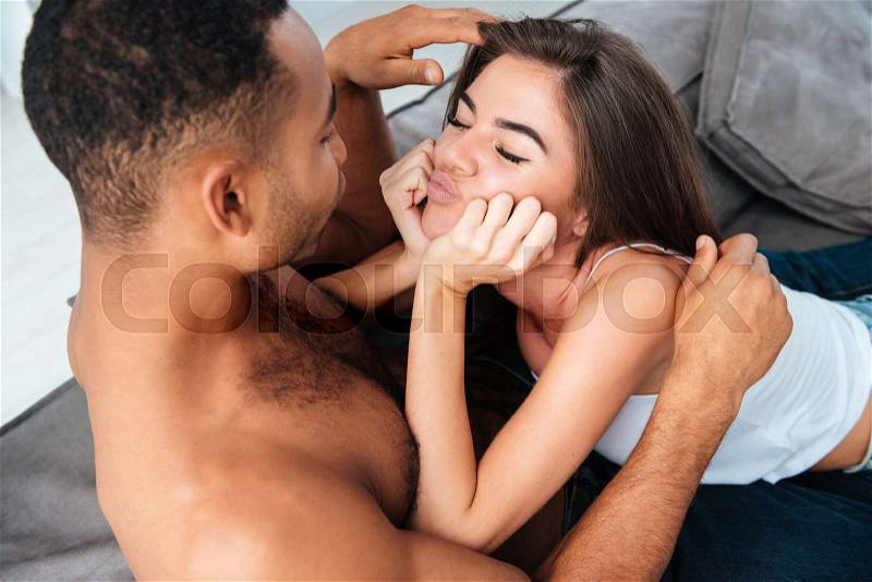Eyes to eyes interracial couple. so happy woman. on bed. guy shirtless, stock photo