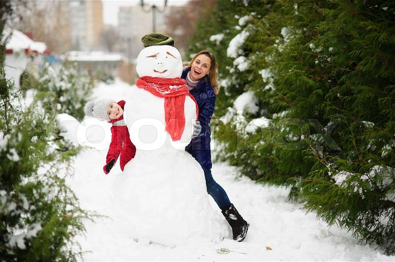 The young woman and her daughter look out because of a big snowman. In the park it is snowing. All earth is covered with fluffy snow. Mother and the daughter cheerfully spend time, stock photo