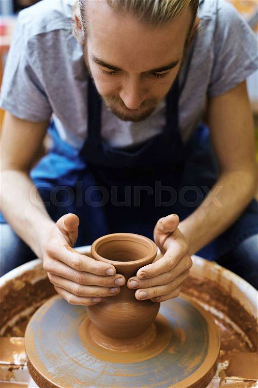 Young potter making clay jug in his workshop, stock photo
