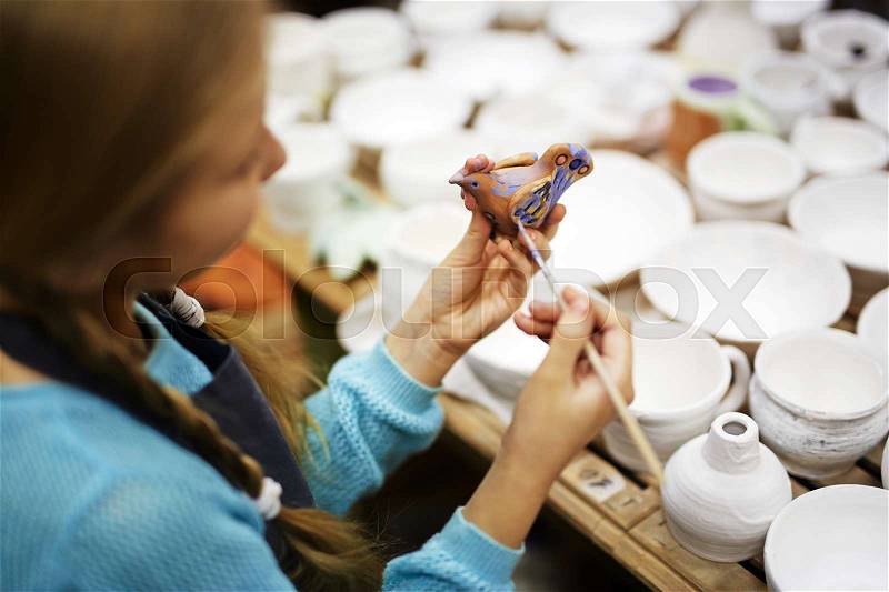 Girl painting clay bird in workshop, stock photo