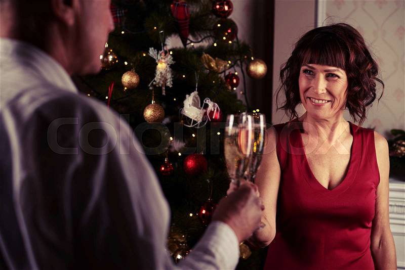 Mid shot of middle-aged couple clinking glasses. Romantic evening at the home. Concept of New Year and Christmas. Celebrating in the familial circle , stock photo