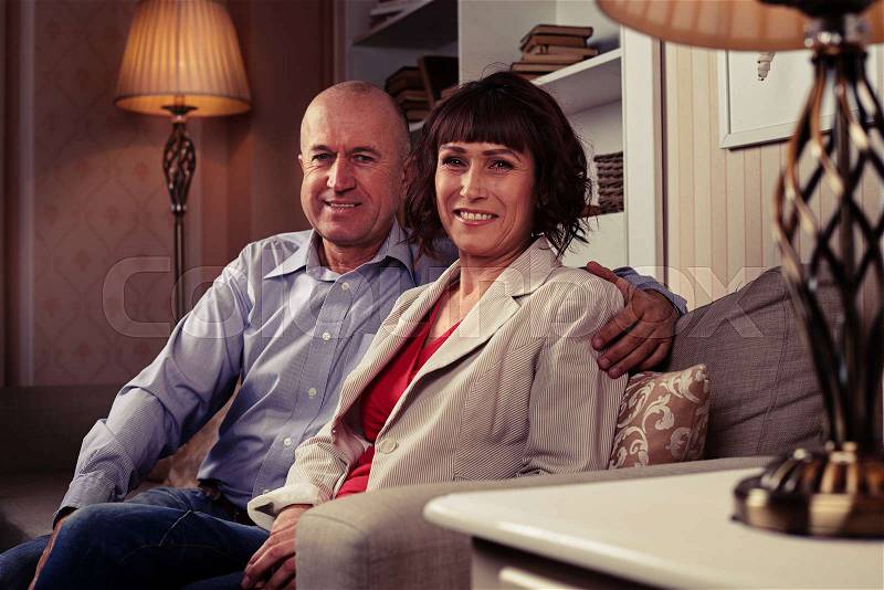 A mid shot a pair of sweethearts sitting on the couch and having their photo taken.A male wearing blue shirt and dark jeans embracing his lady, stock photo