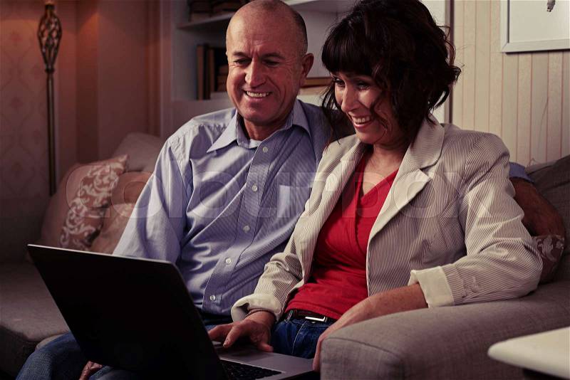 Side mid shot of an elderly pair watching in laptop on the umber settee. Man and woman dressed mainly in classics, stock photo