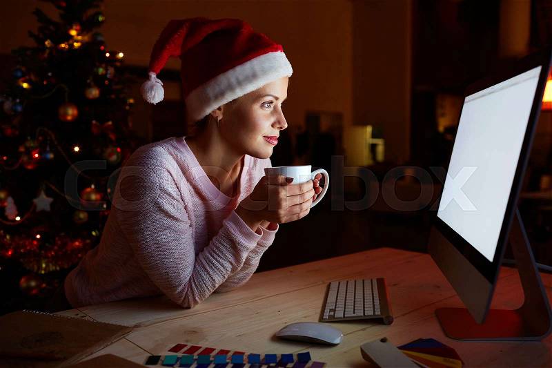 Santa female with cup of hot drink watching movie alone on xmas night, stock photo