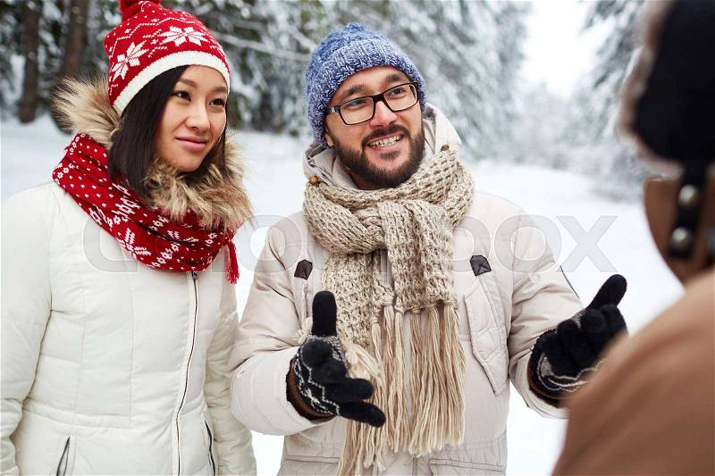 Young man in winterwear explaining how to find road to passer-by, stock photo