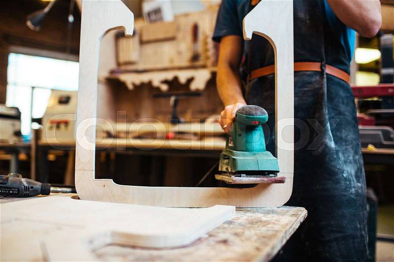 Woodworker grinding wooden workpiece in workshop, stock photo