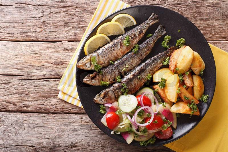 Grilled sardines with roasted potatoes and fresh vegetable salad close-up on a plate. Horizontal view from above , stock photo