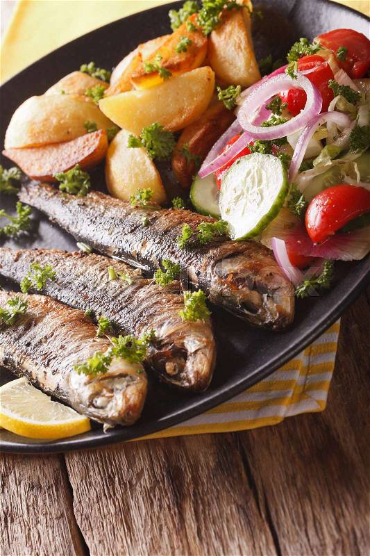Fried sardines with potatoes and fresh vegetable salad close-up on a plate. Vertical\, stock photo