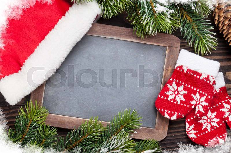 Christmas chalkboard, mittens, santa hat and fir tree on wooden table. Top view with copy space for your text, stock photo