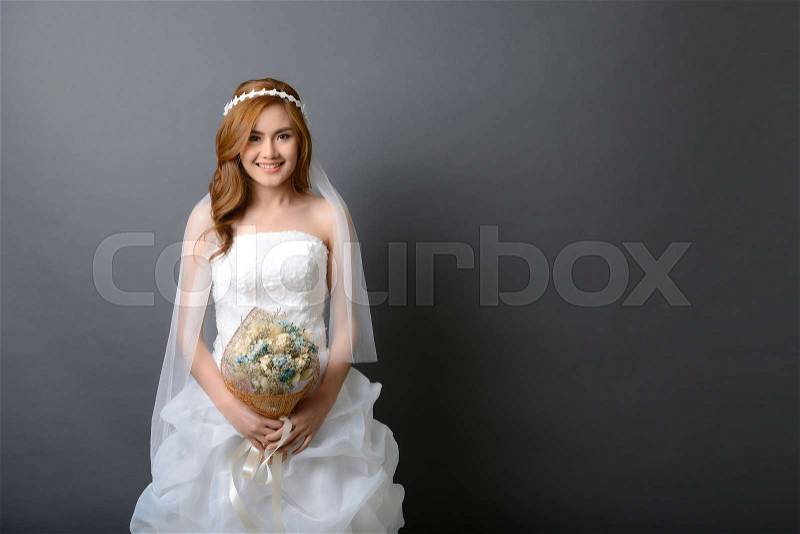 Beautiful young asian bride in wedding dress with flower bouquet, studio shot, stock photo