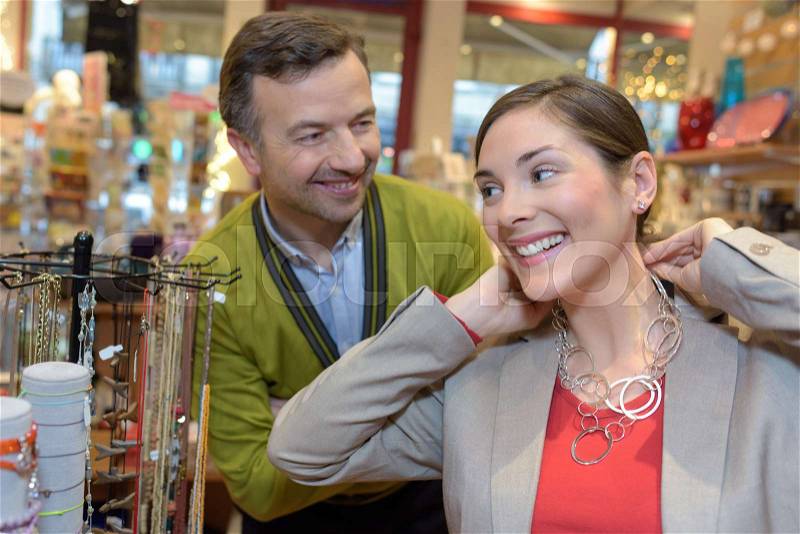 Man attaching necklace to girls neck in retail store, stock photo