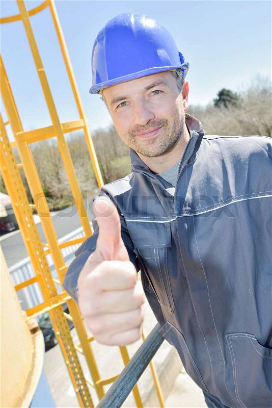 Happy construction worker gesturing thumbs up outdoors, stock photo