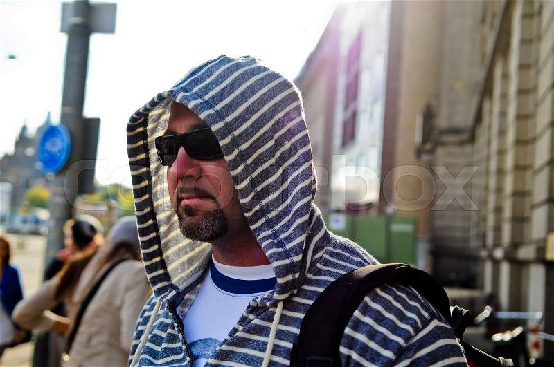 Middle age man with backpack wearing a hood traveling the city, stock photo