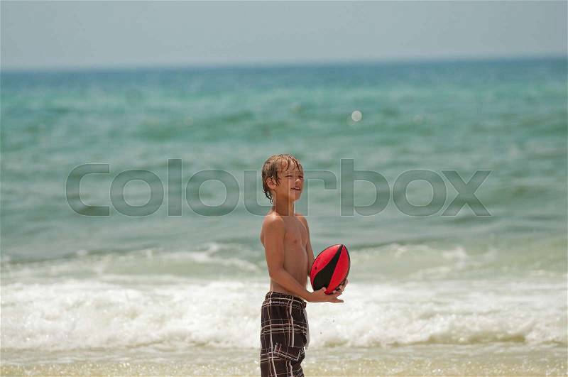 Adorable little boy in swimsuit catching a football on the beach in Florida, stock photo