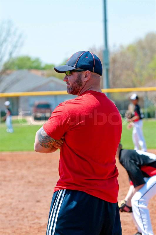 Muscular and handsome baseball coach at first base line looking at batter, stock photo