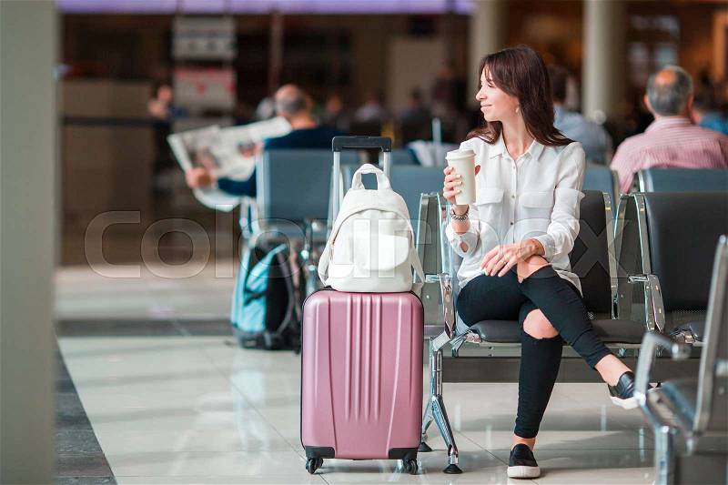 Young woman with coffee in an airport lounge waiting for flight aircraft, stock photo