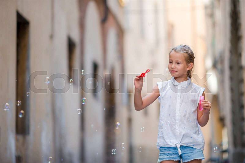 Adorable little girl outdoors blowing soap bubbles in european city. Portrait of caucasian kid enjoy summer vacation in Italy, stock photo