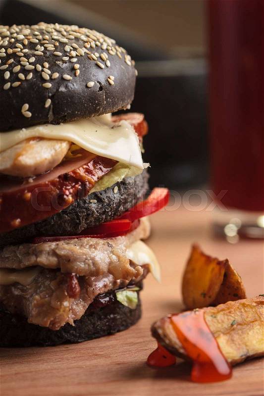 Concept: restaurant menus, healthy eating, homemade, gourmands, gluttony. Trendy burger with four meats in black bun with ingredients, drinks and potato wedges on messy vintage wooden background, stock photo