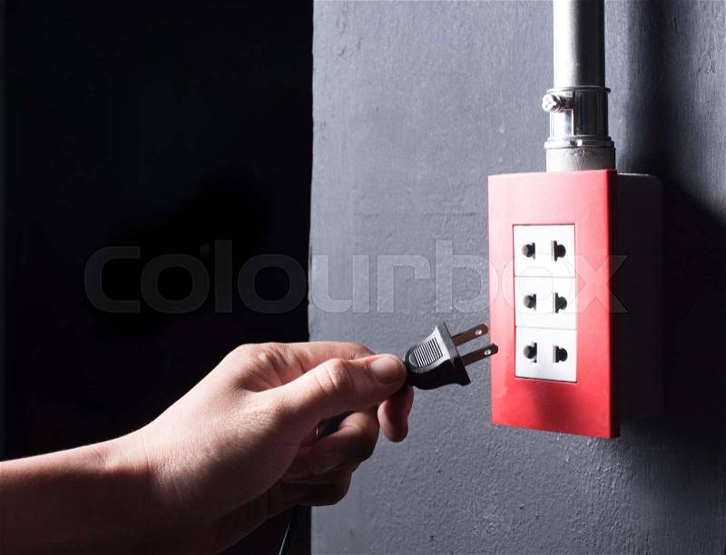Hand inserting unplug or plugged electrical plug into outlet over dark background, stock photo