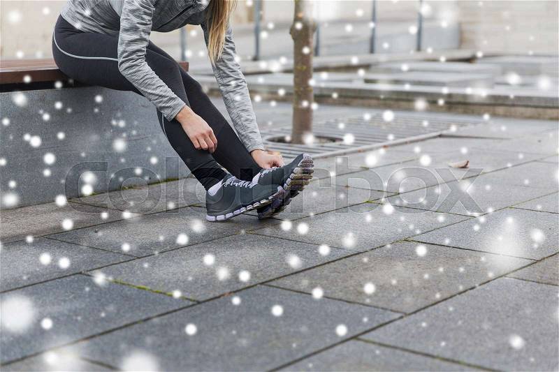 Fitness, sport, people and healthy lifestyle concept - close up of young sporty woman tying shoes outdoors over snow, stock photo