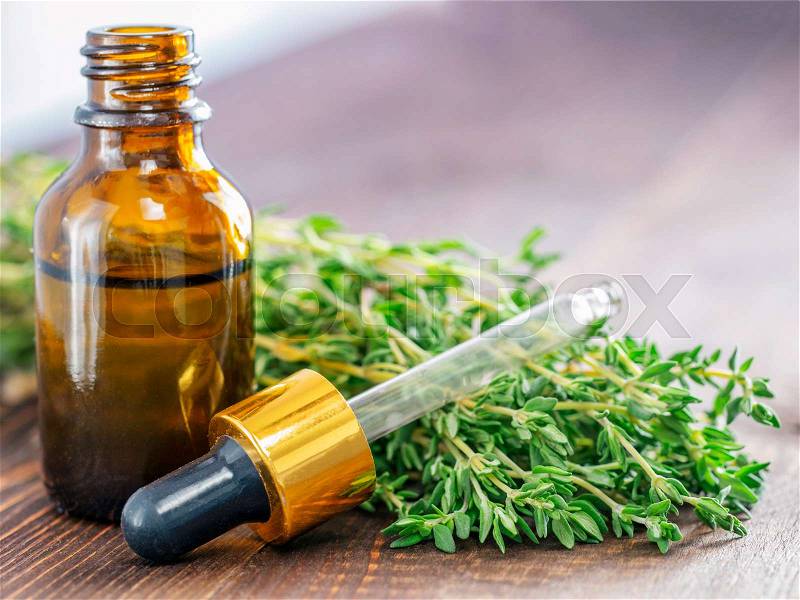Thyme essential oil and dark glass bottle with pipette and fresh thyme on dark brown wooden background with copy space, stock photo