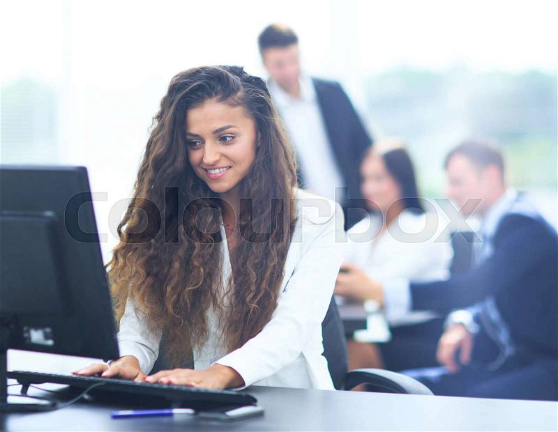 Happy young businesswoman looking behind and her colleagues working at office, stock photo