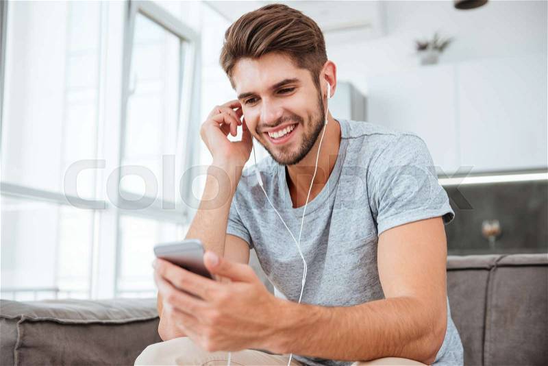 Portrait of happy man listening to music while sitting on sofa and chatting, stock photo