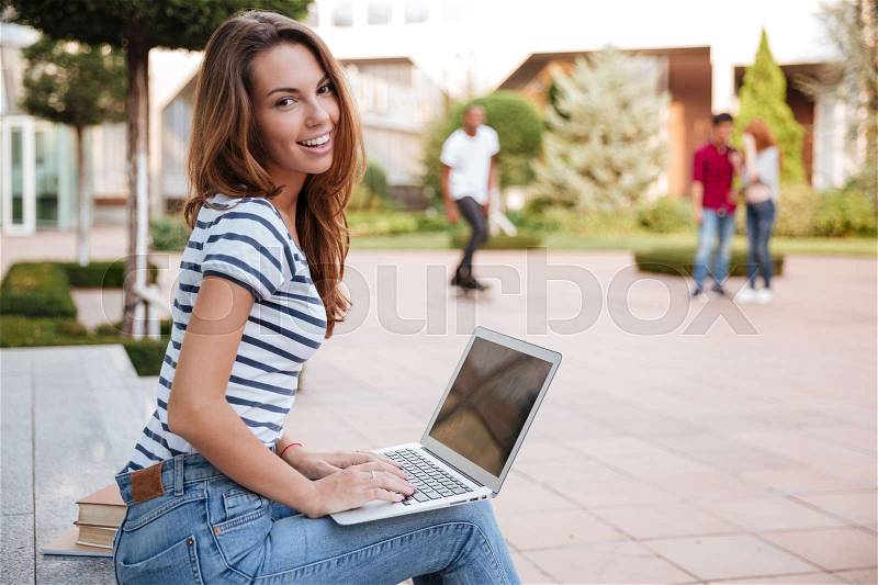Portrait of smiling cute young woman working with laptop outdoors, stock photo