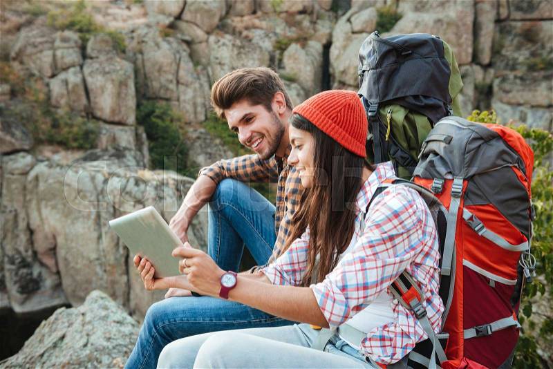 Adventure couple with tablet near the canyon. sitting at rock. side view, stock photo