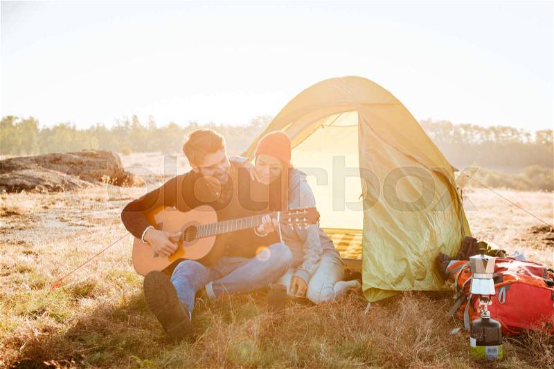 Young beautiful couple having good time with guitar near camping tent, stock photo