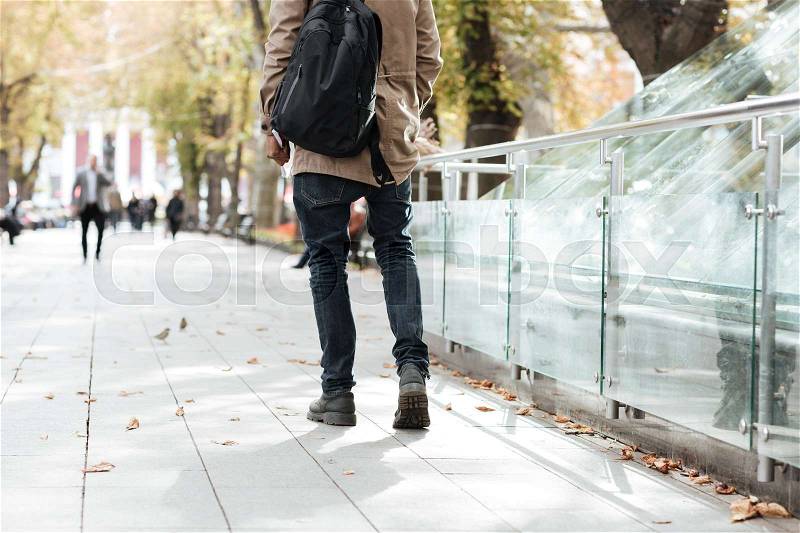 Cropped photo of young african walking man wearing backpack along a street, stock photo