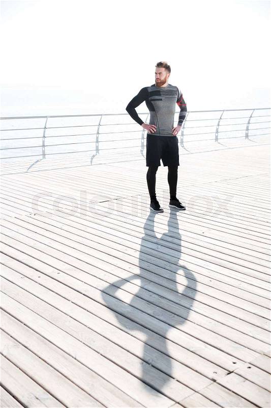 Full length runner near the sea. looking away. arms at hips, stock photo