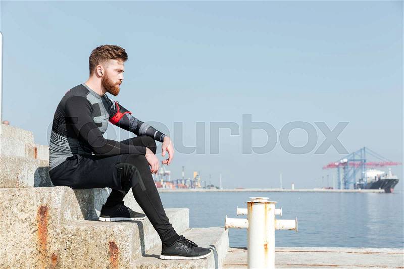 Young runner sitting on stairs near the sea. looking away, stock photo