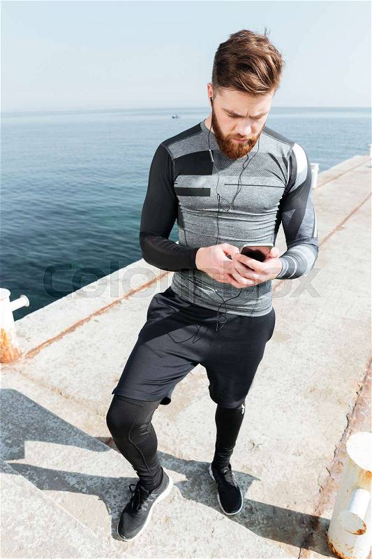 Sportsman with phone near the sea. full length image. looking at phone, stock photo
