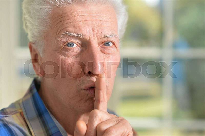 Portrait of senior man presses his finger on mouth asks for silent, stock photo