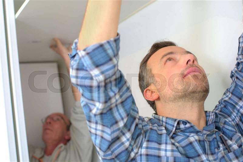 Men fitting plasterboard ceiling, stock photo