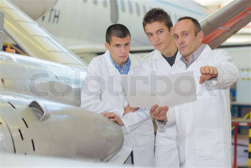 Three men in airport hangar looking at paperwork, stock photo