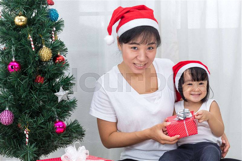 Asian Chinese mother and daughter sitting next to Christmas tree to celebrate Christmas and New Year, stock photo
