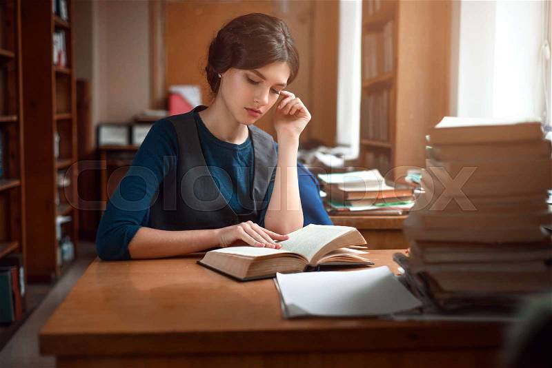 Portrait of clever student reading a book in university library, stock photo