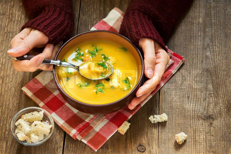 Woman hands holding bowl of vegetable soup with parsley and croutons over wooden background - healthy winter vegetarian food, stock photo