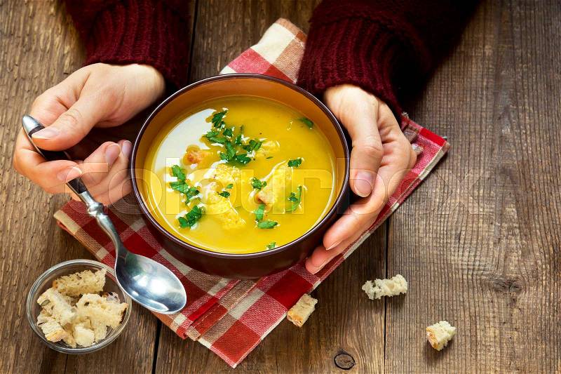 Woman hands holding bowl of vegetable soup with parsley and croutons over wooden background - healthy winter vegetarian food, stock photo