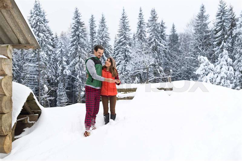 Young Couple Using Smart Phone Snowy Village Wooden Country House Man And Woman Online Messaging Winter Snow Resort Cottage Holiday Vacation, stock photo