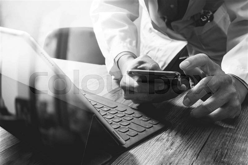 Smart medical doctor hand working with smart phone,digital tablet computer,stethoscope eyeglass,on wood desk,black white, stock photo