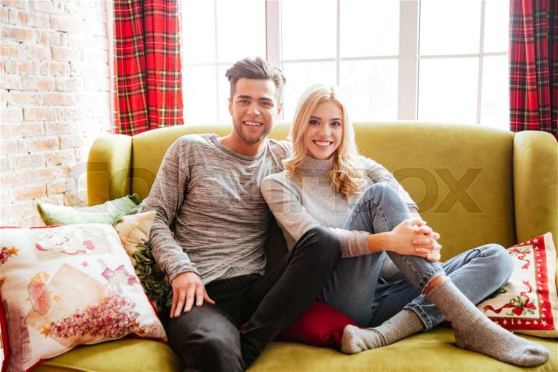 Young couple in sweaters on sofa in house. looks at camera, stock photo